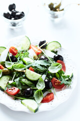Salad with black Olives, cherry Tomatoes, Cucumber and Rocket on bright Background. Close up.