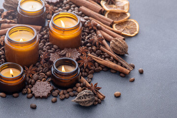 Fototapeta na wymiar Soy scented candle in a jar. Coffee beans, anise, cinnamon spices. The candles are burning. Dark background