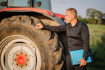 Valmiera, Latvia - August 17, 2024 - A man stands beside a tractor tire in a field, holding a...