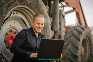 Valmiera, Latvia - August 17, 2024 - A man is smiling and using a laptop while sitting beside a tractor tire outdoors.