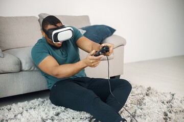 Black guy with virtual reality glasses sitting on a carpet in living room