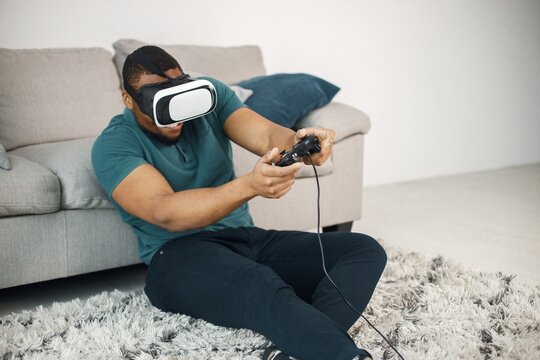 Fototapeta Black guy with virtual reality glasses sitting on a carpet in living room