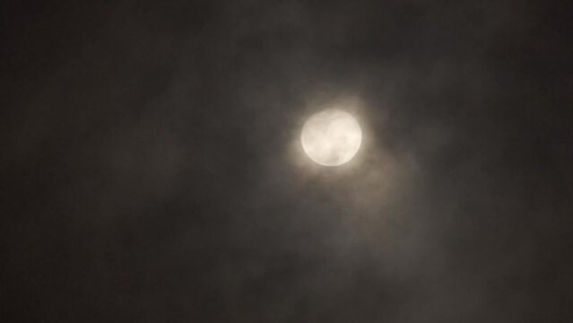 The full moon in the night sky is partially veiled by passing clouds, adding an ethereal quality to the scene. The shifting mist creates a sense of mystery and depth, with the moon's light peeking.