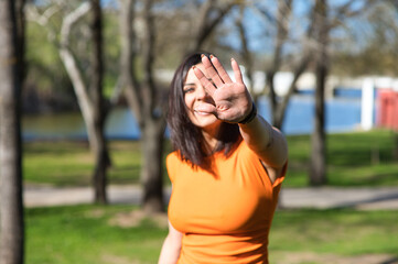 Pretty young woman, brunette and orange dress puts her hand in front of her face to protect...