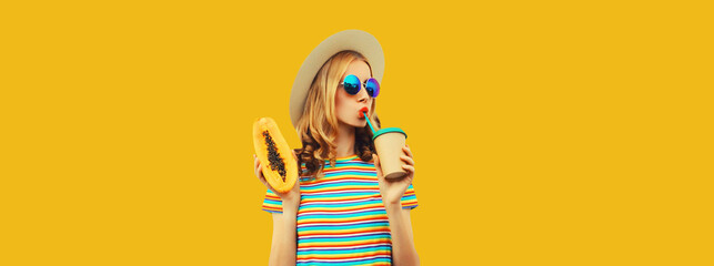 Summer portrait of stylish young woman with papaya fruit drinking fresh juice on yellow background