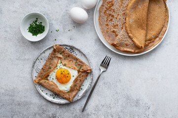 Homemade buckwheat crepes. Galettes Bretonnes with cheese and fried egg on a grey background. Traditional French cuisine.