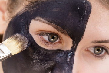 Female applying black mud facial mask - 784513240