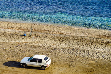Car and fishing pole at the shore of sea.