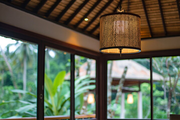 close-up of ceiling lampshade with large windows and white ceiling, forest in background