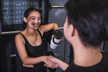 A friendly young asian woman shakes the hand of a new male friend at the gym. Approaching a beautiful woman.