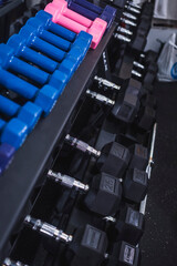 A detailed view of neatly arranged rubberized and black hex dumbbells on a rack at a fitness center, highlighting gym equipment.
