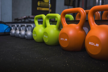 Close-up of a variety of colorful kettlebells lined up on a gym floor, highlighting weights for fitness and strength training.