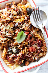 Baked fusilli pasta with cherry tomatoes, olives and mozzarella cheese. Bright wooden background....