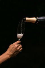 Hands pouring champagne in glass on black  background. Waiter pouring white sparkling wine. Party celebration concept. © Kajornsiri