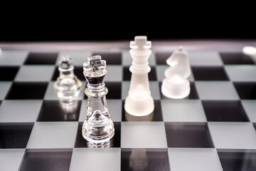 glass chess pieces on a chessboard on black background , selective focus on king chess piece...