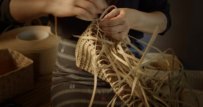An Asian female artisan who is a rural villager weaving folk baskets and women's bags  made from leftover paper band to sell as extra income in the community shop.

