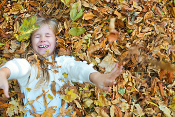 Kid plays in autumn park. Child throwing yellow and red leaves. Little girl with oak and maple...