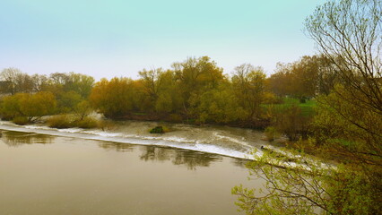 Fototapeta premium Blick auf Wehr mit Wasserfall an der Lahn in Limburg mit grünen Bäumen entlang des Ufers