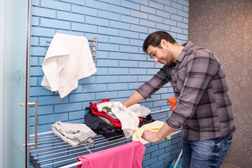 A young man dries clothes on a dryer after washing in the bathroom. Caring husband doing housework	