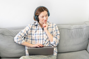 Young attractive woman sitting on the couch and working on laptop at home. Online education and distance working concept