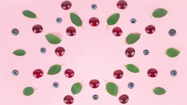 4k Ripe cherries, blueberries and green leaves arranged in a circle on a pink background. Berries and leaves are blinking. Concept of berries season and proper nutrition. Stop motion animation.
