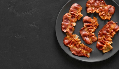 Roasted bacon on plate over black stone background with free space