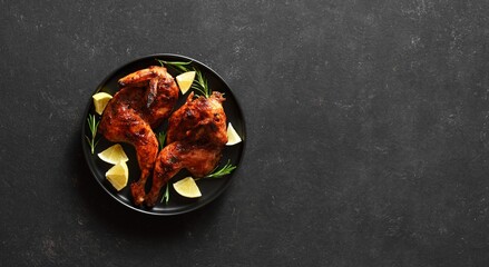 Grilled half chicken with lemon and rosemary on plate over dark stone background with copy space.