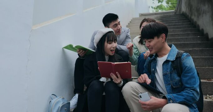 Four Asian university students sit on the campus steps discussing their coursework, simultaneously documenting their conversation.