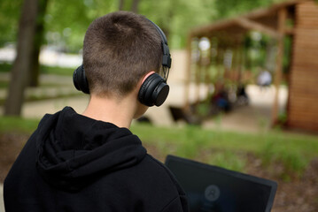 A young guy in headphones sits on a bench in the park with a laptop. Zielona Gora, Poland -...