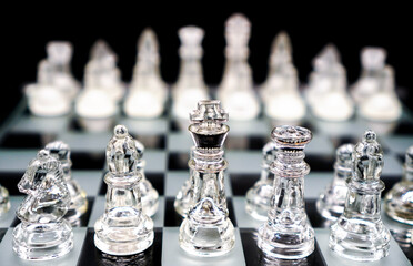 glass chess pieces on chessboard on black background represent competition and strategy concept , selective focus on top of front row pieces
