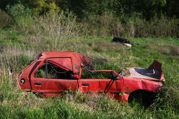 Rusty and broken red abandoned car in the outdoors. Old abandoned rusty car without wheels on the side of the road - 784588043