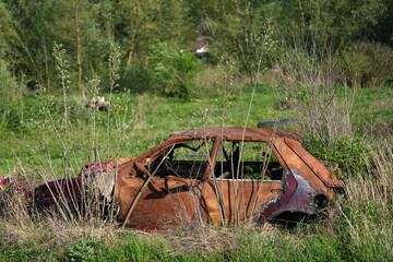 Rusty and broken red abandoned car in the outdoors. Old abandoned rusty car without wheels on the side of the road - 784588056