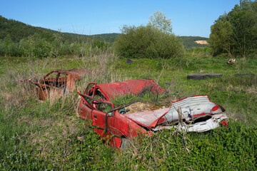 Rusty and broken red abandoned car in the outdoors. Old abandoned rusty car without wheels on the side of the road - 784588081