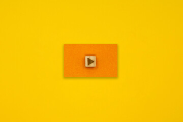 黄色い背景の中央にあるオレンジ色の四角い再生マークのアイコン