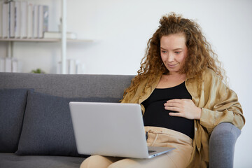 pregnant woman sitting on sofa and working on laptop computer in the office