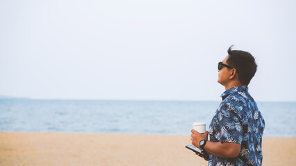 Tourists wearing sunglasses use smartphones and holding a cup of coffee on the beach