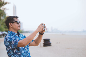 Tourists wearing sunglasses use smartphones to take pictures of the sea and beach.
