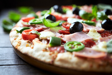 Pizza with ham, mozzarella cheese, cherry tomatoes, green and jalapeno pepper, black olives and fresh basil. Dark background. Close up.	