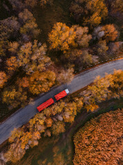 Red tipper truck on street road highway transportation. Semi-truck autumn countryside aerial view.