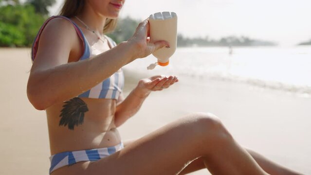 Happy Woman Squeezing Water-resistant Suncream From Bottle. Caucasian Female Applying Spf On Skin At Sea. Tanned Fit Girl In Bikini Sitting On Sand, Putting Waterproof Sunscreen On Leg At The Seaside.