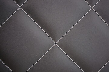 White contrast thread on a black leather car seat close-up