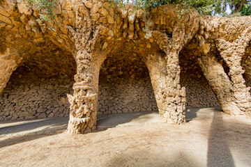 Viaduct in Laundry Room Portico with columns made of masonry with stone wall in background in Parc Guell, architectural work of Gaudi, sunny day in Barcelona, Catalonia, Spain