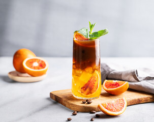 Coffee with orange juice (bumble) in a tall glass with ice and mint on a wooden board on a light...