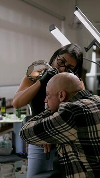 Woman tattooing a man's head, doing a scalp process in her studio