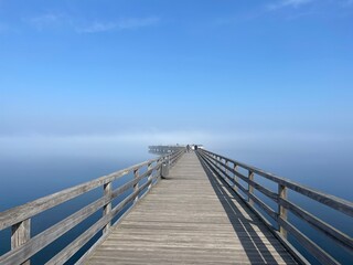 long wooden bridge over the sea in morning fog with sunshine