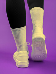 Close-up of female legs in white sneakers, back view, purple background