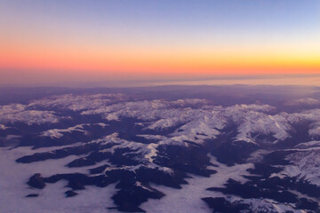 View out of an airplane window of a snow-covered mountain range at sunset