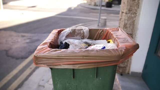 Close-up shot of a filled green coloured rubbish bin. Top shot of a plastic bin with bags inside.