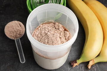 Whey protein powder and milk in a shaker on a dark background with plastic measuring spoon and bananas, process of making protein shake drink