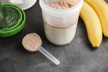Whey protein powder with a chocolate flavor in a plastic measuring spoon, shaker with a milk and...